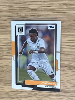 Samlarbild Vinícius Jr. Real Madrid - Säljer en samlarbild från Panini Donruss Soccer med Vinícius Jr. i Real Madrids vita matchställ. Kortet har FIFA-logga och Optic Donruss-märkning, med färger i vitt, svart och orange. Perfekt för dig som gillar fotboll och samlarkort.