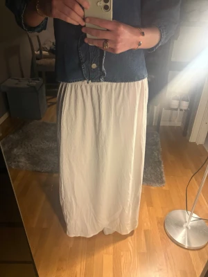Vit långkjol med resår i midjan - Säljer en enkel och stilren vit långkjol med resår i midjan. Kjolen har en rak och luftig passform och är gjord i ett lätt tyg som ger en avslappnad känsla. Jättefint skick använd 1 gång