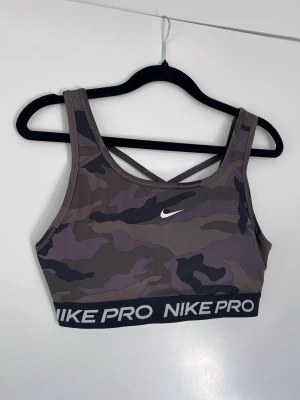 Nike Pro sport-bh i camo mönster, stl M - Nike sport-bh med korsade axelband och funktionsmaterial i ryggen. Khakigrön. Ger bra med stöd, urtagbart ilägg!