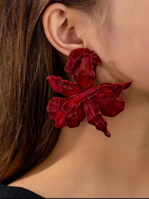 Stora röda blomörhängen - Unika statementörhängen i form av stora blommor i blank röd plast. Örhängena har en tredimensionell design med vågiga blomblad som ger en cool och iögonfallande look. Perfekta för dig som vill sticka ut och addera färg till din outfit.