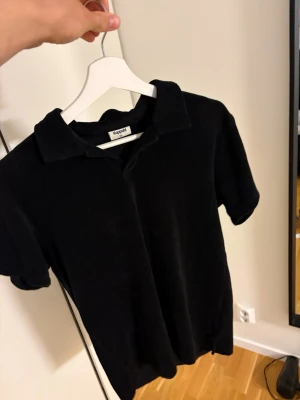 Svart polotopp från Kappahl - En svart Frotté piké ifrån Kappahl. Stilren tröja med skön passform. Perfekt för sommarens varma dagar. Inga defekter på plagget. Storleken är 170, men sitter som en S