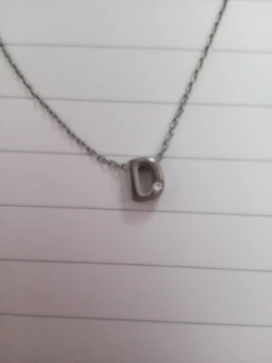 Silverhalsband med bokstav D - Snyggt halsband i silverfärg med ett hänge i form av bokstaven D. Hänget har en liten sten. Är ganska anpassningsbar i storleken som visas på bilden. Är använd men i gott skick.