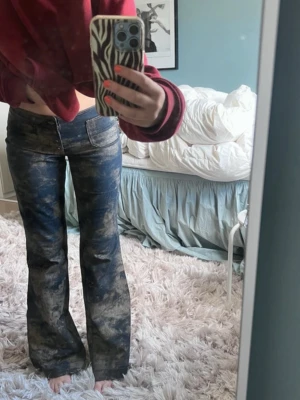 Blå bootcut jeans med tvättad look - Säljer ett par blå bootcut jeans med unik tvättad effekt som ger en cool vintage vibe. Jeansen har normal passform i storlek 36 och klassiska fickor både fram och bak. Perfekta för dig som vill sticka ut med din stil! Passar mig som är 168!
