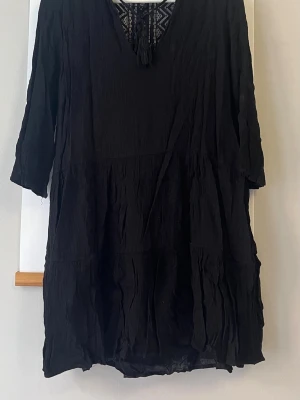 Svart boho-klänning med spetsdetaljer - Svart kortklänning i boho-stil med trekvartsärm och v-ringning. Klänningen har fina spetsdetaljer upptill och ett lätt, vågigt tyg som ger en avslappnad känsla. Perfekt för dig som gillar en ledig men ändå stilren look.