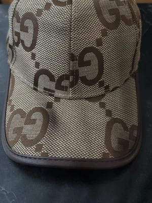 Beige keps med GG-mönster - Snygg beige keps  med det klassiska GG-monogrammet i brunt över hela kepsen. Tillverkad i bomull och polyester med detaljer i elastan. Perfekt accessoar för en trendig och exklusiv look.