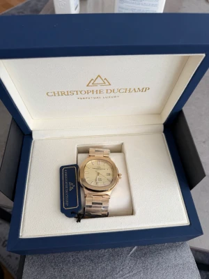 Christophe Duchamp - Stilren guldfärgad klocka från Christophe Duchamp med metallarmband och elegant urtavla. Klockan levereras i originalbox och har en klassisk, lyxig design som passar perfekt till dig som vill sticka ut med accessoarerna. Helt nytt, kvitto finns, möts hellre upp o säljer än att frakta.