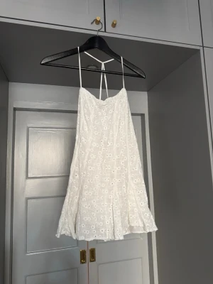 ZARA vit kort klänning med broderade blommor - Superfin vit kort klänning med tunna axelband och broderade blommor. Klänningen har en lätt utsvängd form och knytning i ryggen. Perfekt för varma dagar och har en romantisk vibe med sitt blommiga mönster. Perfekt till midsommar