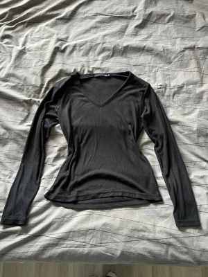 Svart ribbad långärmad topp  - Säljer en svart ribbad långärmad topp från lager 157 i storlek M. Toppen har en snygg v-ringning och är figurnära i modellen. Perfekt att styla med jeans eller kjol för en clean look 🥰🩷