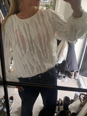 Vit plisserad blus med struktur - Trendig vit blus med plisserad struktur och vågiga detaljer. Blusen har rund halsringning och långa, luftiga ärmar med resår vid ärmslut. Perfekt för dig som gillar en stilren men ändå unik look.