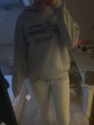 Grå hoodie med blått tryck - Säljer en grå hoodie med blått tryck av bilar på bröstet. Hoodien har en klassisk huva och är gjord i mjukt material, perfekt för en avslappnad stil. Passar dig som gillar streetwear och vill ha något bekvämt och snyggt.