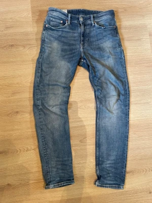 Blå slim jeans  - Klassiska blå jeans med raka ben och fem fickor. Jeansen har en snygg tvättad look med slitningar speciellt på fickorna. Perfekta för en avslappnad stil.