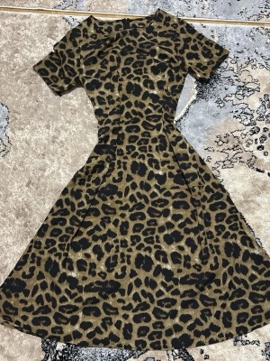 Leopardmönstrad klänning med kort ärm - Snygg klänning med leopardmönster i bruna och svarta toner. Modellen har korta ärmar, markerad midja och utsvängd kjol som ger en feminin siluett. Perfekt för dig som vill sticka ut med ett djurmönstrat plagg.