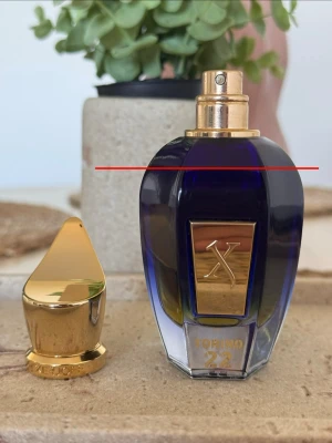 Xerjoff Torino 22 parfym 50ml - Det finns 45 ml kvar. Lyxig parfymflaska från Xerjoff i modellen Torino 22. Flaskan är djupblå med gulddetaljer och har en elegant, geometrisk form. Locket är spetsigt och guldfärgat med märkets logga ingraverad. Perfekt för dig som gillar exklusiva dofter och snygg design. Tyvärr ingen presentation. Nen dofter är vad man ska vara ut efter den håller dagar och doftar så unik och bra