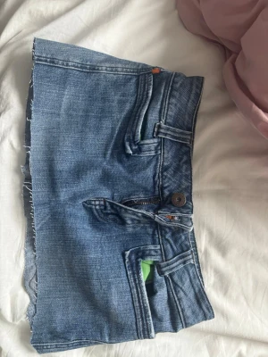 Blå jeanskjol med rå kant - LÄS!! Trendig kort jeanskjol i blå denim med rå, avklippt kant och klassiska fickor både fram och bak. Kjolen har knapp- och dragkedjestängning samt detaljer i orange. Perfekt för dig som gillar en edgy och avslappnad stil. Jag har klippt dessa själv kortare för den var för lång innan. 