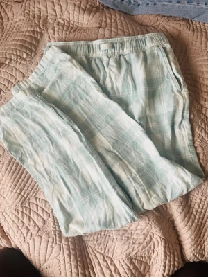 Ljusblå rutiga pyjamasbyxor Kappahl - Mysiga pyjamasbyxor från Kappahl i ljusblått och vitt rutmönster. Byxorna har resår i midjan och är gjorda i mjukt, tunt tyg som passar perfekt för att chilla hemma. Klassisk och avslappnad passform.