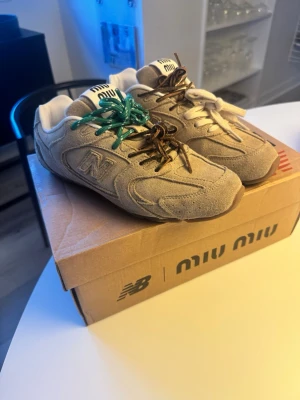 Beige Miu Miu x New Balance sneakers - Unika beige sneakers i mocka från Miu Miu x New Balance med flera olika färger på skosnörena – grönt, brunt och vitt. Kopior som jag köpt på Vinted. Passar inte mig . Ena bruna skosnöret har gått av så jag har knutigt det , se bild 