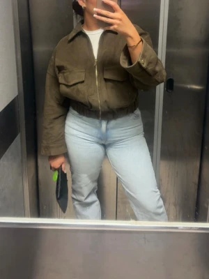 Grön Brun mocka jacka från Zara - Snygg brun bomberjacka i mocka-look med dragkedja framtill och två stora bröstfickor. Jackan har en croppad passform med resår i midjan och breda ärmar med knappdetalj vid mudden. Perfekt för dig som vill ha en trendig och avslappnad stil.