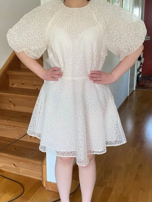 Vit kort klänning med puffärmar - En sprillans ny crèmefärgad kort klänning med puffiga kortärmar och blommigt spetsmönster! 🌸Köpte för att ha på studenten men den var för beige. Alla etiketter är på och pris går självklart att diskutera! Perfekt för sommarens alla tillfällen!