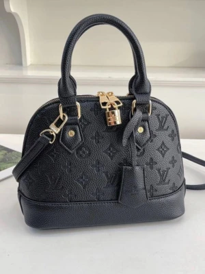 svart handväska - Snygg svart handväska  i präglat läder med klassiskt monogrammönster. Väskan har guldfärgade metalldetaljer, dubbla handtag och avtagbar axelrem. Dragkedja med lås och stilren form som ger en lyxig känsla.Oanvänd 