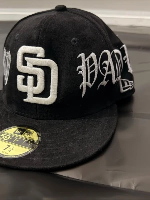 Svart New Era SD Padres keps - Snygg svart keps från New Era 59FIFTY med broderad SD-logga och texten 'PADRES' i vitt framtill. Klassisk flat peak och strukturerad passform. Perfekt för dig som gillar sportig streetstyle.