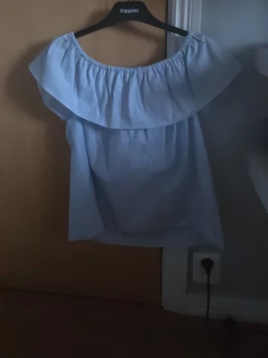 Blåvit offshoulder topp hm - Söt offshoulder topp från hm i ljusblått och vitt med smala ränder. Toppen har en bred volang runt axlarna och är ärmlös, perfekt för varma dagar. Tillverkad i mjuk bomull för en skön känsla.