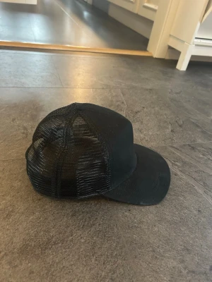 Svart Stetson truckerkeps - Snygg svart truckerkeps med böjd skärm och mesh-paneler på sidorna och bak för extra ventilation. Använd 3 gånger och i ny skick. Klassisk och stilren design som passar till det mesta. Justerbar storlek baktill för perfekt passform.