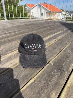 Svart keps från Civare - Snygg svart keps från Civare med böjd skärm och broderad text 'CIVARE EST. 2026' framtill. Kepsen har en klassisk sexpanel-design och justerbar rem bak. Materialet ser ut att vara bomull med en tvättad vintage-look.