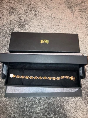 Guldarmband från Kejsar - 8mm Snyggt guldfärgat armband från Kejsar med tvinnad repdesign. Armbandet har en robust låsning och levereras i en exklusiv svart ask med Kejsar-logga. Perfekt accessoar för att lyfta din stil med en lyxig touch.