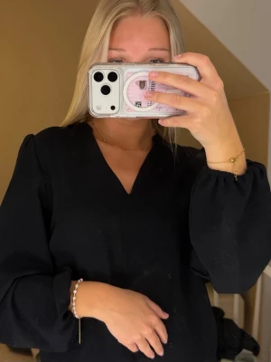 Svart blus med v-ringning - Stilren svart blus med v-ringad hals och långa puffärmar. Blusen har en enkel och klassisk design som passar till många olika outfits. Materialet ser ut att vara mjukt och lätt, perfekt för en trendig look.