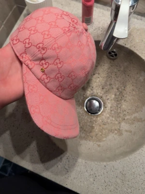  Gucci keps  - Säljer en snygg rosa keps från Gucci med det klassiska GG-monogrammet över hela kepsen. Kepsen har böjd skärm och är tillverkad i ett tygmaterial som känns både trendigt och lyxigt. Perfekt accessoar för att lyfta din outfit. Helt ny