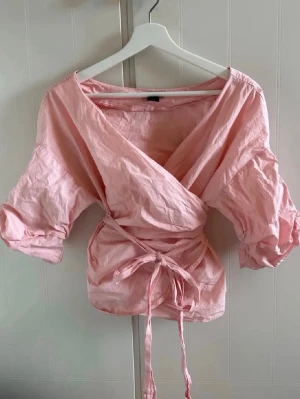Rosa omlottblus från Lindex - Söt rosa omlottblus från Lindex med knytband!! Varan har knappt används och har inga tecken på användning💝 Blusen är från Lindex och i storlek S!! Priset går att diskutera vid snabb affär💝💝