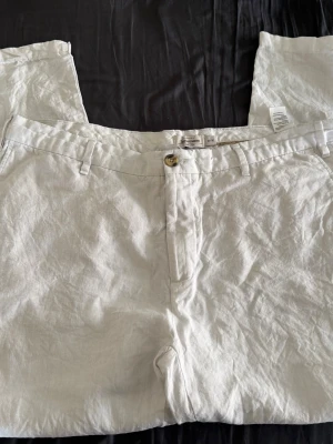 Vita linnebyxor från Dressmann - Snygga vita linnebyxor från Dressmann med klassisk passform och raka ben. Byxorna har hällor för bälte, knapp och dragkedja framtill samt sidfickor. Perfekta för en chill och luftig stil under varma dagar.
