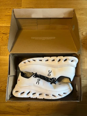 On cloud skor  - Säljer ett par vita On Cloudnova sneakers med unik sula och svarta detaljer. Skorna har låg profil, ventilerande mesh och cool design med On-logga på sidan. Perfekta för dig som vill sticka ut med stilrena och bekväma sneakers.