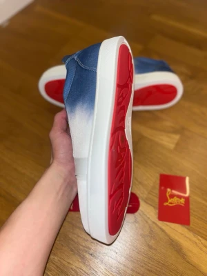 Christian Louboutin blåvita jeans modellen  - Snygga sneakers från Christian Louboutin i blåvitt tyg med cool ombre-effekt. Skorna har klassisk låg modell, vita snören och den ikoniska röda sulan. Perfekta för dig som vill sticka ut med stilrena detaljer och exklusiv känsla.
