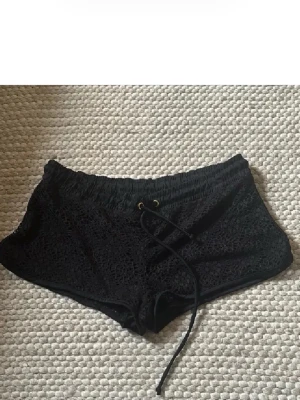 Svarta lågmidjade virkade shorts med snörning - Snygga svarta lågmidjade shorts med virkad look och snörning i midjan. De har elastisk midja och är perfekta för varma dagar. Stilen är loose och materialet känns lätt och luftigt.
