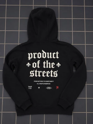 Svart hoodie från Hoodrich - Svart hoodie från Hoodrich med stor vit text 'HOODRICH' framtill och 'product of the streets' i gotisk stil på ryggen. Röd detalj och texten 'From Nothing To Something' både fram och bak. Klassisk känguruficka och huva. Perfekt för streetwear-stilen.