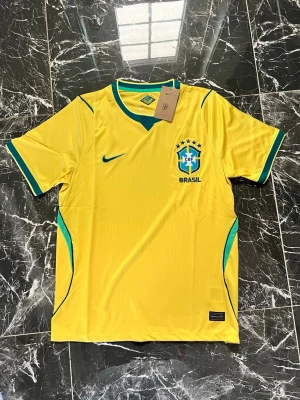 Brasilien matchtröja Nike gul - Gul Brasilien matchtröja från Nike med gröna och blå detaljer. Tröjan har korta ärmar, rund halsringning och är tillverkad i ett lätt, ventilerande funktionsmaterial. Brasil-logga och Nike Swoosh på bröstet. Perfekt för fotboll och sport.