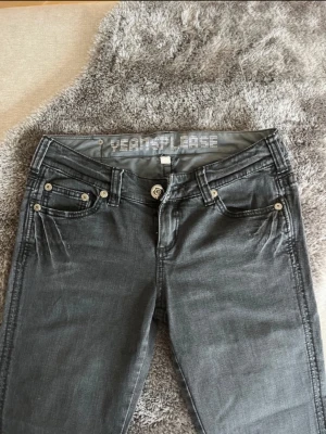 Grå jeans från Yeah!Please - Snygga grå jeans från Yeah!Please med raka ben och klassisk femficksmodell. Jeansen har silverfärgade nitar och knappdetaljer samt ett coolt tryck i midjan. Perfekta för dig som gillar en stilren och avslappnad look.