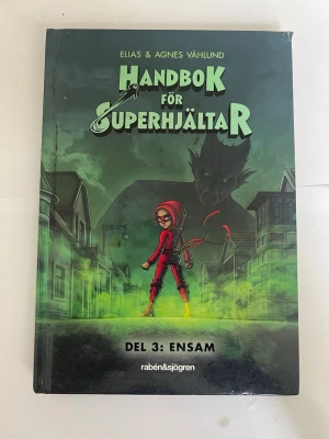 Handbok för superhjältar del 3: Ensam - Handbok för superhjältar del 3: Ensam av Elias & Agnes Våhlund. Boken har ett färgstarkt omslag med en tecknad tjej i röd dräkt och huva, mot en mystisk stadsmiljö i gröna och svarta toner. Perfekt för dig som gillar spännande äventyr och superhjältar.