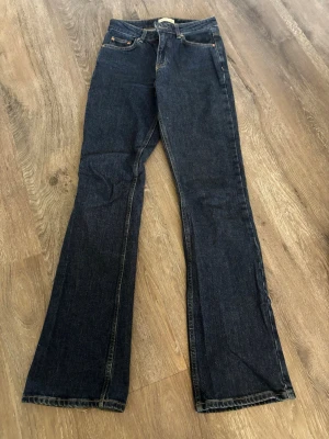 Mörkblå bootcut jeans - Snygga mörkblå bootcut jeans med klassisk femficksdesign och kontrastsömmar. Jeansen har en något utsvängd passform nedtill och är tillverkade i kraftigt denimtyg. Perfekta för en avslappnad och trendig look.