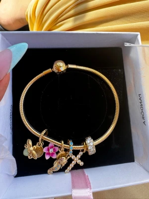 Pandora armband med charms  - Säljer mitt helt nya Pandora armband med berlocker, var i Stockholm och fick en impuls att jag ville köpa det men när jag kom hem ångrade jag mig och den närmsta butiken ligger 4 timmar bort om jag ska lämna tillbaka det. Så testar att sälja det istället. Allt som medföljer är:   - Snake chain bracelet - 1199kr - Clip charm - 799kr - Cross dangle charm - 549kr  - Seahorse dangle charm - 899kr - Glow in the dark firefly dangle charm - 899kr - Disney Moana Flower dangle charm - 899kr  (5244kr) 