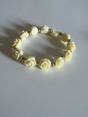 Elastiskt armband med rosor - Sött armband med vita pärlor formade som rosor och små silvriga mellanpärlor. Armbandet är elastiskt och passar de flesta handleder. Perfekt för dig som gillar romantiska detaljer och vill ha något unikt till din stil.