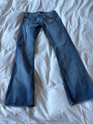 Blå bootcut jeans  - Säljer ett par blå bootcut jeans från MSG70 med snygga detaljerade bakfickor och knappar. Jeansen har en klassisk femficksmodell och är gjorda i denim med den perfekta tvätten. Perfekta för dig som vill ha ett par snygga och trendiga med samtidigt unika jeans 