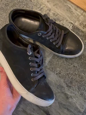 Lanvin storlek 40 - Snygga svarta sneakers med lågt skaft, svarta skosnören och vit sula. Ovandelen är i textil med tåparti i blankare material och metallöljetter för snörningen. Perfekta för en clean och stilren look.