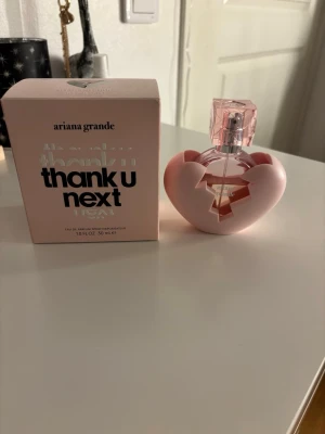 Ariana Grande Thank U Next parfym - Säljer en Ariana Grande Thank U Next parfym, 30 ml. Flaskan är rund och rosa med ett genomskinligt lock och står i en unik rosa hjärtformad hållare. Förpackningen är ljusrosa med svart text. Perfekt för dig som gillar söta och fruktiga dofter.