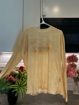 Ljusgul långärmad topp Acne Studios - Långärmad topp från Acne Studios i en ljusgul nyans. Toppen har rund halsringning och ett diskret präglat tryck med texten 'STOCKHOLM PARIS' framtill. Perfekt för en avslappnad och trendig look.