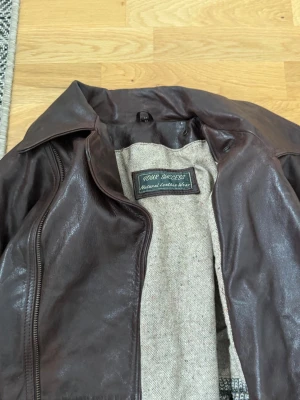 Mörkbrun skinnjacka  - Snygg mörkbrun skinnjacka från Your Success med klassisk krage och dragkedja framtill. Jackan har två fickor med lock och en mjuk, ljus innerfodring. Perfekt för dig som vill ha en tidlös och cool look.