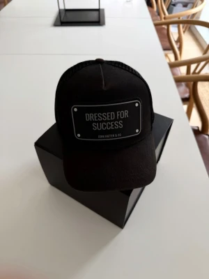 John Hatter & Co – “Dressed for Success” Truckerkeps - Säljer en stilren och populär keps från John Hatter & Co med det klassiska budskapet “Dressed for Success”. En snygg svart truckermodell som passar lika bra till vardags som för att sätta en personlig touch på outfiten.  Svart färg Justerbar storlek baktill Mycket gott skick Originaldesign från John Hatter & Co  Kepsen är sparsamt använd och i fint skick utan anmärkningar.