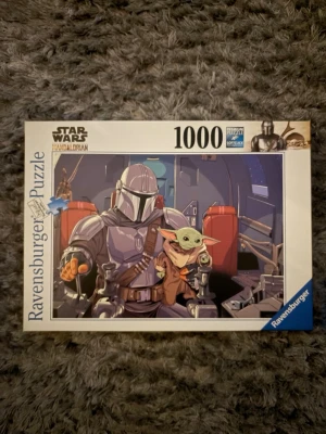 Star Wars Mandalorian pussel 1000 bitar - Säljer ett Ravensburger pussel med Star Wars Mandalorian-motiv. Pusslet har 1000 bitar och motivet visar Mandalorian och Grogu i ett rymdskepp. Kartongen är vit med färgglad illustration på framsidan. Perfekt för dig som gillar Star Wars och pussel. Alla bitar finns.