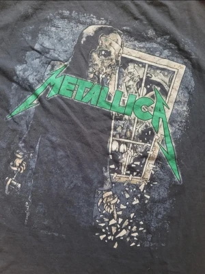 Svart Metallica t-shirt - Svart t-shirt med stort Metallica-tryck på framsidan i grönt och vitt. Klassisk passform och rund hals, perfekt för dig som gillar bandtröjor. Den är lite använd men inte sliten. 